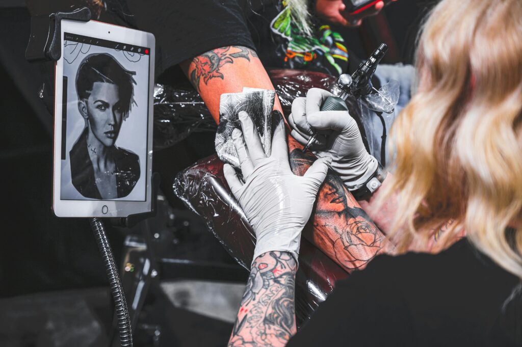 Tattoo artist creating a detailed arm tattoo using modern tools in a studio setting.