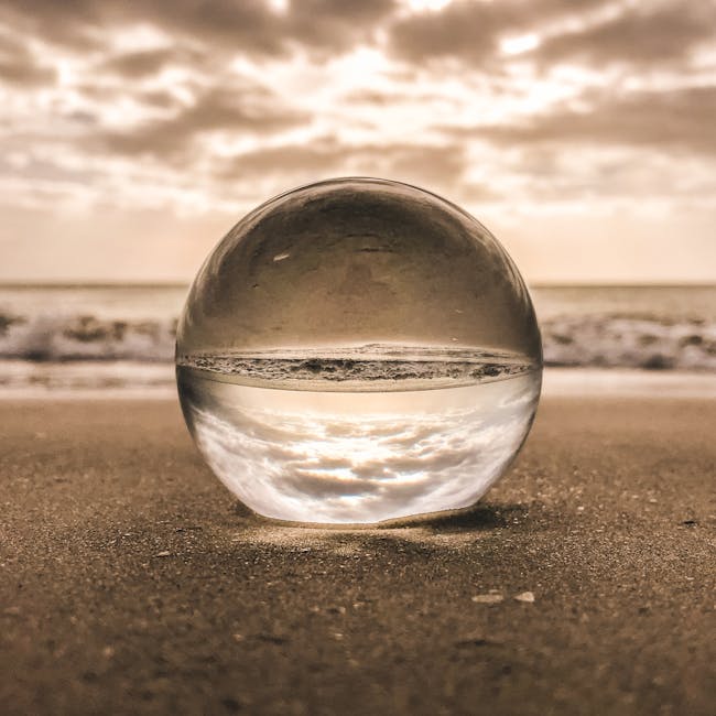 A glass sphere reflecting the sky and ocean on a sandy beach at sunset in Bonita Springs, FL.